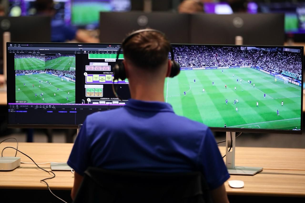 An analyst in headphones coding a football match in an Angles MarkUp, the match full screen beside it.